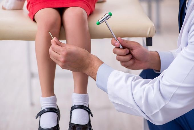 Paediatric orthopaedic specialist assessing a toddler's walking pattern and knee alignment during a gait evaluation.